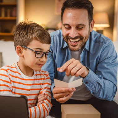 Baba ve oğul evde tabletle birlikte hediye kutusundan kart okurlar.