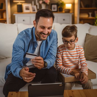 Babası kredi kartını elinde tutarken oğlu paketi elinde tutarken internetten tablet almış.