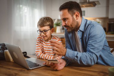 Çocuk mutfaktan dizüstü bilgisayar alırken, yetişkin beyaz bir babanın elinde kredi kartı var.