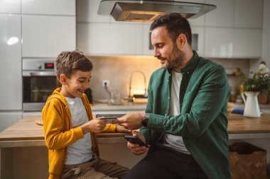 Oğlu ve babası evde oturuyor ve kredi kartıyla cep telefonundan online alışveriş yapıyorlar.