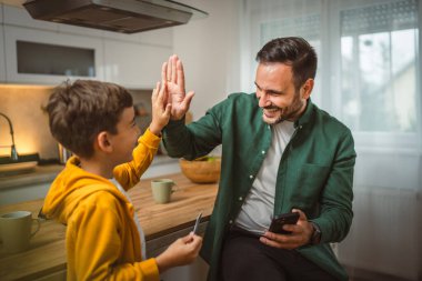 Oğlu ve babası evde oturuyor ve kredi kartıyla cep telefonundan online alışveriş yapıyorlar.