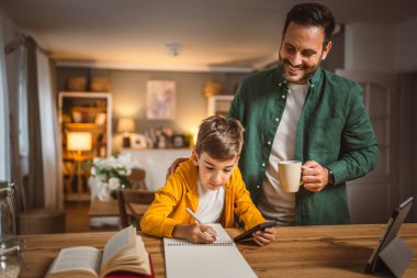 Evde cep telefonundan notları kopyalayan bardaklı baba yardımcısı oğul.