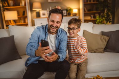 Baba ve oğul evdeki video görüşmesi için cep telefonu kullanıyor.
