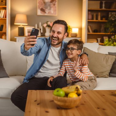 Baba ve oğul evdeki video görüşmesi için cep telefonu kullanıyor.