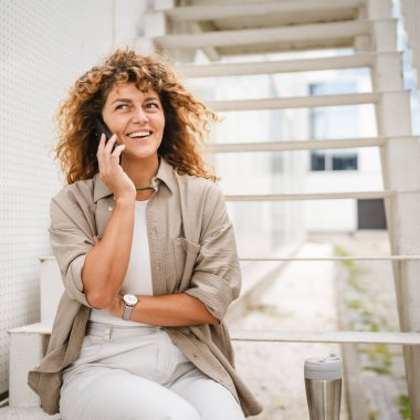 Yetişkin kadın merdivenlerde oturur ve cep telefonuyla konuşur.