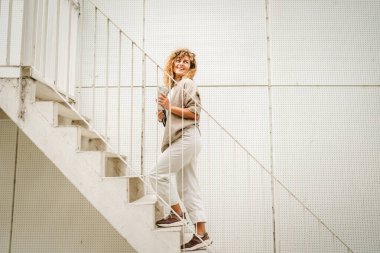 Yetişkin bir kadın merdivenlerden çıkıp tablet ve termos kaplarını tutar.