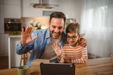 Baba ve oğul açık doğum günü hediyesi ve masada tabletle bir video çağrısı var.