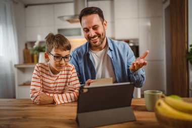 Baba ve oğul açık doğum günü hediyesi ve masada tabletle bir video çağrısı var.