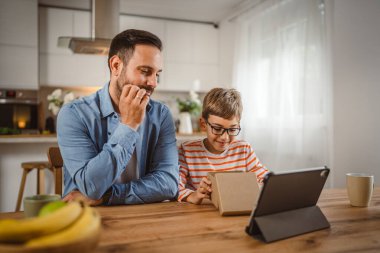 Baba ve oğul açık doğum günü hediyesi ve masada tabletle bir video çağrısı var.