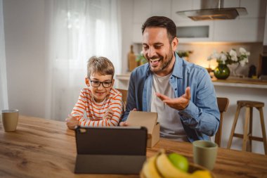 Baba ve oğul açık doğum günü hediyesi ve masada tabletle bir video çağrısı var.