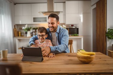 Baba ve oğul açık doğum günü hediyesi ve masada tabletle bir video çağrısı var.