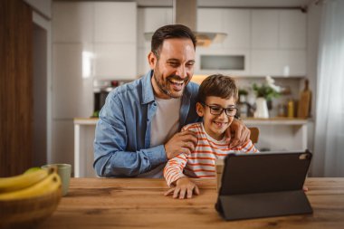 Baba ve oğul açık doğum günü hediyesi ve masada tabletle bir video çağrısı var.