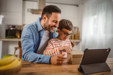 Baba ve oğul açık doğum günü hediyesi ve masada tabletle bir video çağrısı var.