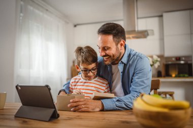 Baba ve oğul açık doğum günü hediyesi ve masada tabletle bir video çağrısı var.