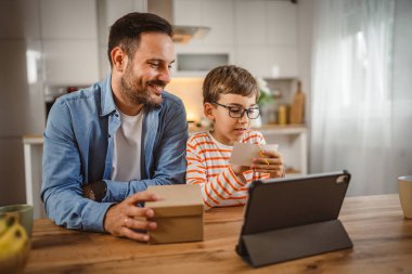 Baba ve oğul evde birlikte kart okuyorlar ve masada tablet var.