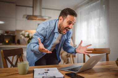 Mutlu adam laptopta iyi haberler okudu. Oğlu arka plandayken evde çalışıyordu.