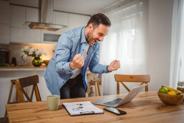 Mutlu adam laptopta iyi haberler okudu. Oğlu arka plandayken evde çalışıyordu.