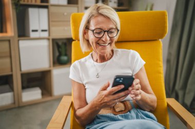 Olgun son sınıf öğrencisi kadın evde oturur ve cep telefonunu mesajlaşma ya da internette gezinmek için kullanır