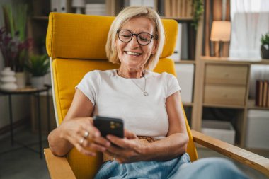 Olgun son sınıf öğrencisi kadın evde oturur ve cep telefonunu mesajlaşma ya da internette gezinmek için kullanır