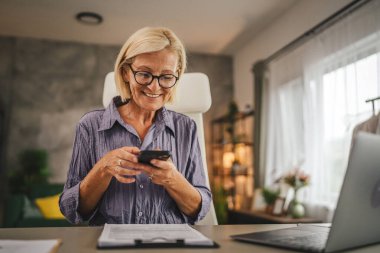 Olgun yaşlı kadın evde çalışır ve sigorta, sözleşme ya da cep telefonuyla belgeyi tarar