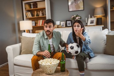 Gergin çift erkek arkadaş ve kız arkadaş futbol maçını futbol topu, bira ve evde patlamış mısırla birlikte izliyorlar.