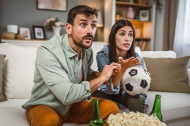 Gergin çift erkek arkadaş ve kız arkadaş futbol maçını futbol topu, bira ve evde patlamış mısırla birlikte izliyorlar.