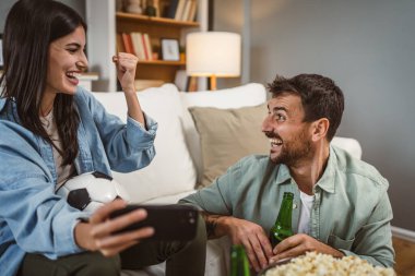 Sevgililer futbol maçı izler ve evde futbol topu, bira ve patlamış mısırla online bahis oynarlar.