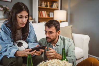 Sevgililer futbol maçı izler ve evde futbol topu, bira ve patlamış mısırla online bahis oynarlar.