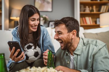 Sevgililer futbol maçı izler ve evde futbol topu, bira ve patlamış mısırla online bahis oynarlar.