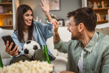 Sevgililer futbol maçı izler ve evde futbol topu, bira ve patlamış mısırla online bahis oynarlar.
