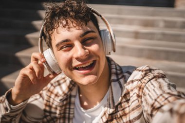 Genç mutlu adamın portresi merdivenlerde kulaklıkla oturuyor.