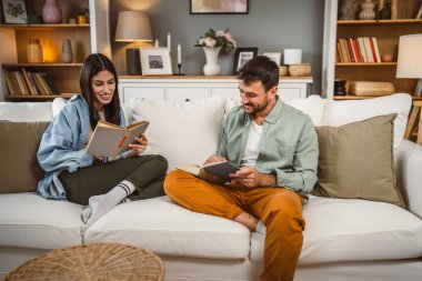 Erkek ve kadın Kafkasyalı yetişkin çift evde kanepe yatağında kitap okuyor.