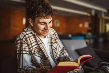 Oturup kitap okuyan genç bir çocuk.