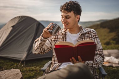 Delikanlı, çadırın önünde otur ve dağda bir kitap oku.