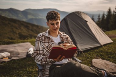 Delikanlı, çadırın önünde otur ve dağda bir kitap oku.
