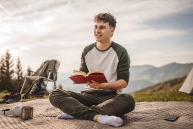 Genç çocuk çadırın önündeki dağda bir kitap okudu.