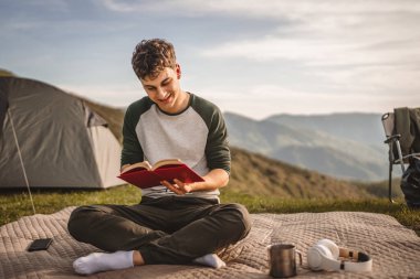 Genç çocuk çadırın önündeki dağda bir kitap okudu.