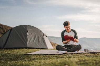Genç çocuk çadırın önündeki dağda bir kitap okudu.