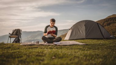 Genç çocuk çadırın önündeki dağda bir kitap okudu.