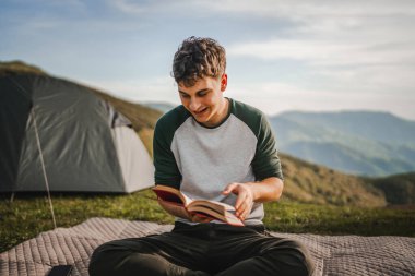 Genç çocuk çadırın önündeki dağda bir kitap okudu.