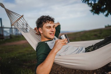 Genç çocuk, dağda bir fincan kahveyle hamakta uzanıyordu.