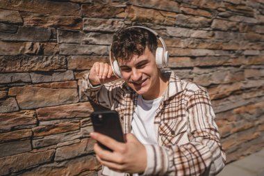 Kulaklıklı genç bir çocuk cep telefonuyla video görüşmesi yapıyor.