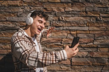 Kulaklıklı genç bir çocuk cep telefonuyla video görüşmesi yapıyor.