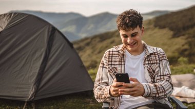 Delikanlı, çadırın önünde otur ve dağda cep telefonu kullan.