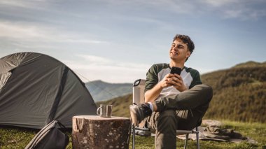 Delikanlı, çadırın önünde otur ve dağda cep telefonu kullan.