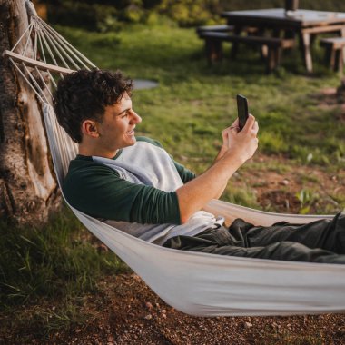 Hamakta uzanmış bir çocuk cep telefonu kamerasıyla fotoğraf çekiyor.