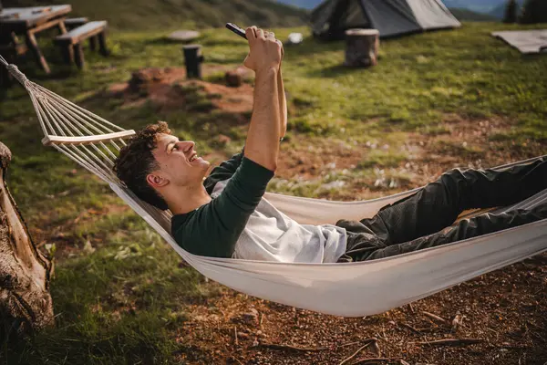 stock image Young adult boy lying down in hammock take a self portrait or video call on mobile phone