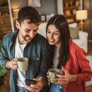 Çift, kahve fincanlarını tutarken cep telefonunu mesaj atmak ya da internette gezinmek için kullanır