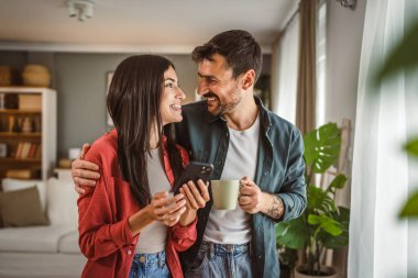 Çift, kahve fincanlarını tutarken cep telefonunu mesaj atmak ya da internette gezinmek için kullanır