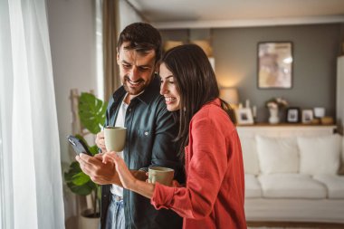 Çift, kahve fincanlarını tutarken cep telefonunu mesaj atmak ya da internette gezinmek için kullanır